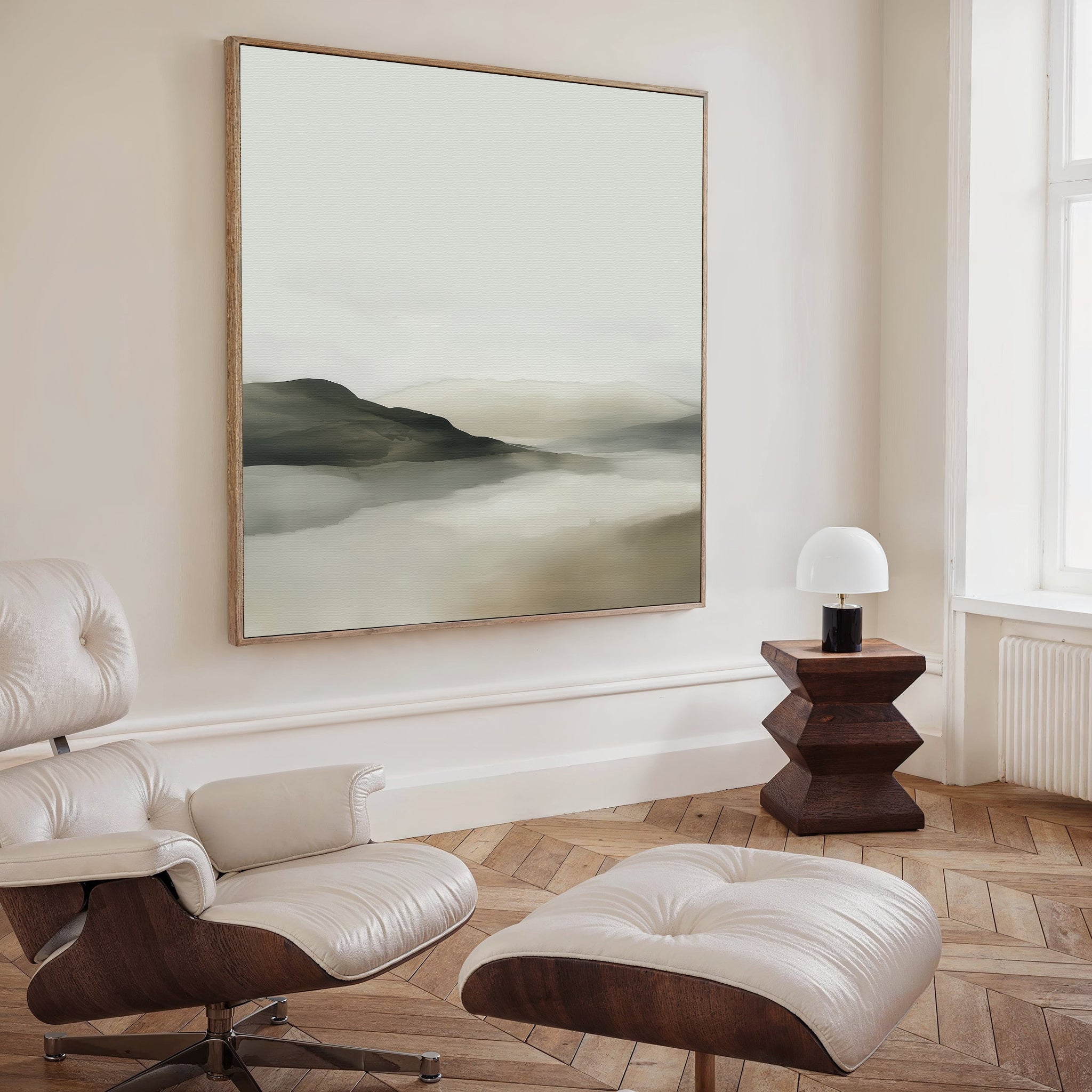 A modern living room with a white leather lounge chair and ottoman, wooden floors, a geometric side table with a small lamp, and minimalist decor featuring the Soft Valley Canvas Art as large wall art above.
