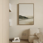 Minimalist living room with a beige sofa, light wooden bookshelf, and the Soft Valley Canvas Art – Vertical, a framed abstract painting of soft hills and misty tones, adding calming minimalist decor to the neutral wall.