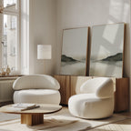 A modern living room features the Soft Valley Set of 2 white, rounded armchairs, a wooden coffee table, and a sideboard with art. Large windows fill the space with light, highlighting the minimalist decor.