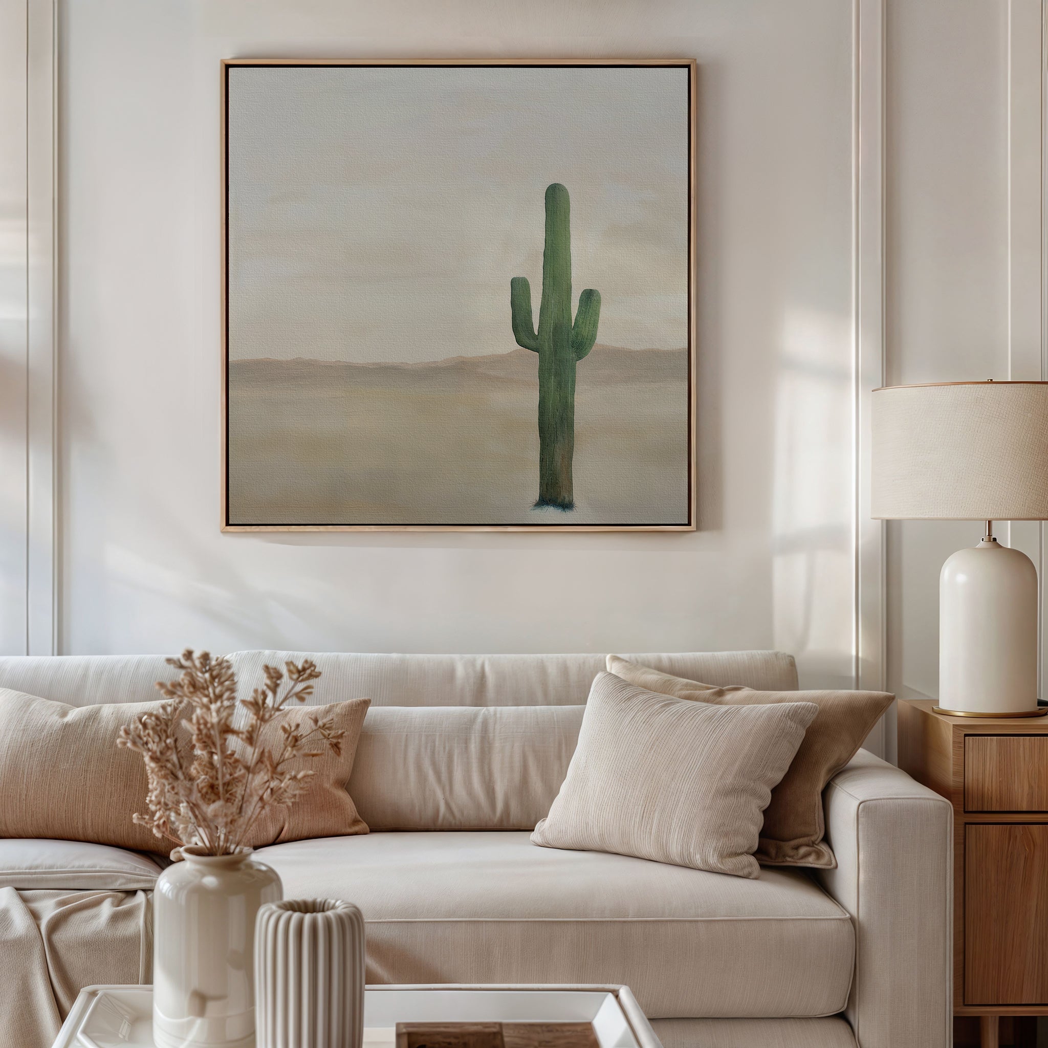 A neutral living room with a beige sofa, cream and tan pillows, a dried floral arrangement in a vase, minimalist decor, and the Solitary Rise Canvas Art hung above the sofa. A table lamp rests on a wooden side table.