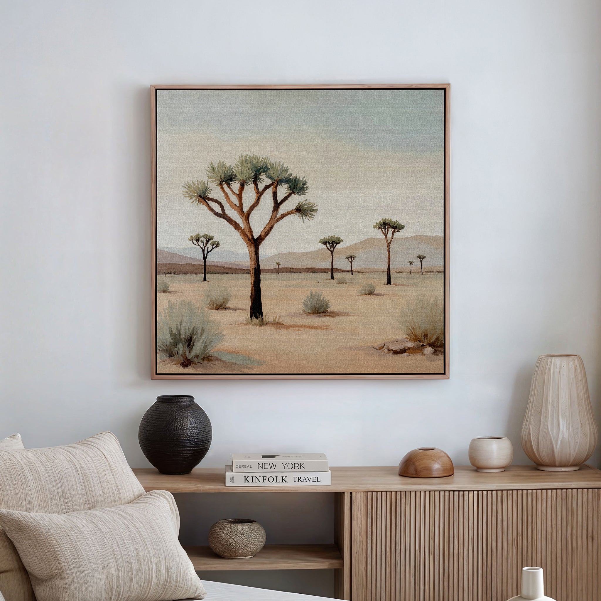 The Sparse Growth Canvas Art, featuring a desert landscape with Joshua trees, hangs above a light wood sideboard with vases and books, bringing nature-inspired decor to this minimalist living room.