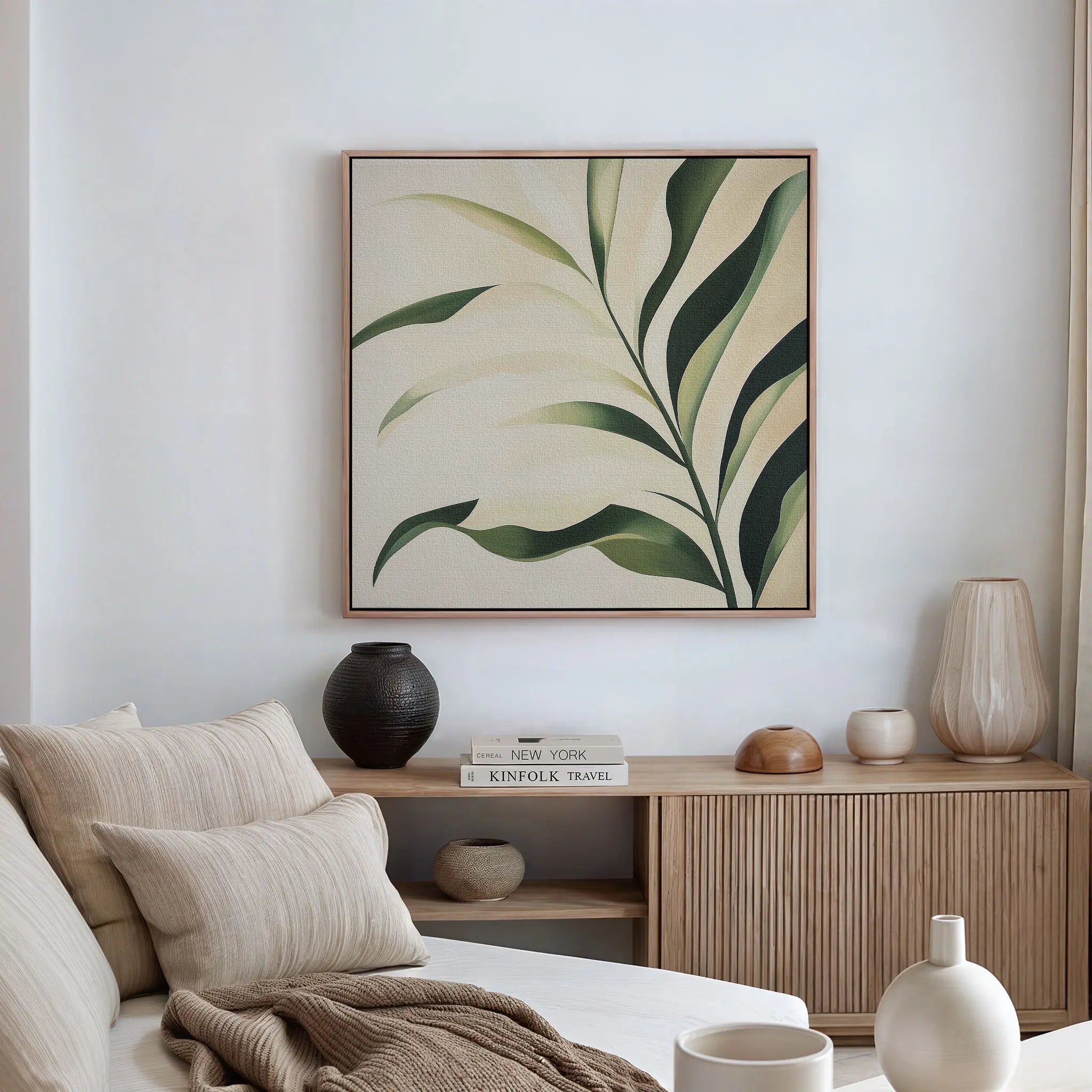 A minimalist living room with a beige sofa, cream pillows, and wooden sideboard is enhanced by the Spring Foliage Canvas Art—a green leaves print that adds a fresh touch to the modern decor on the white wall.
