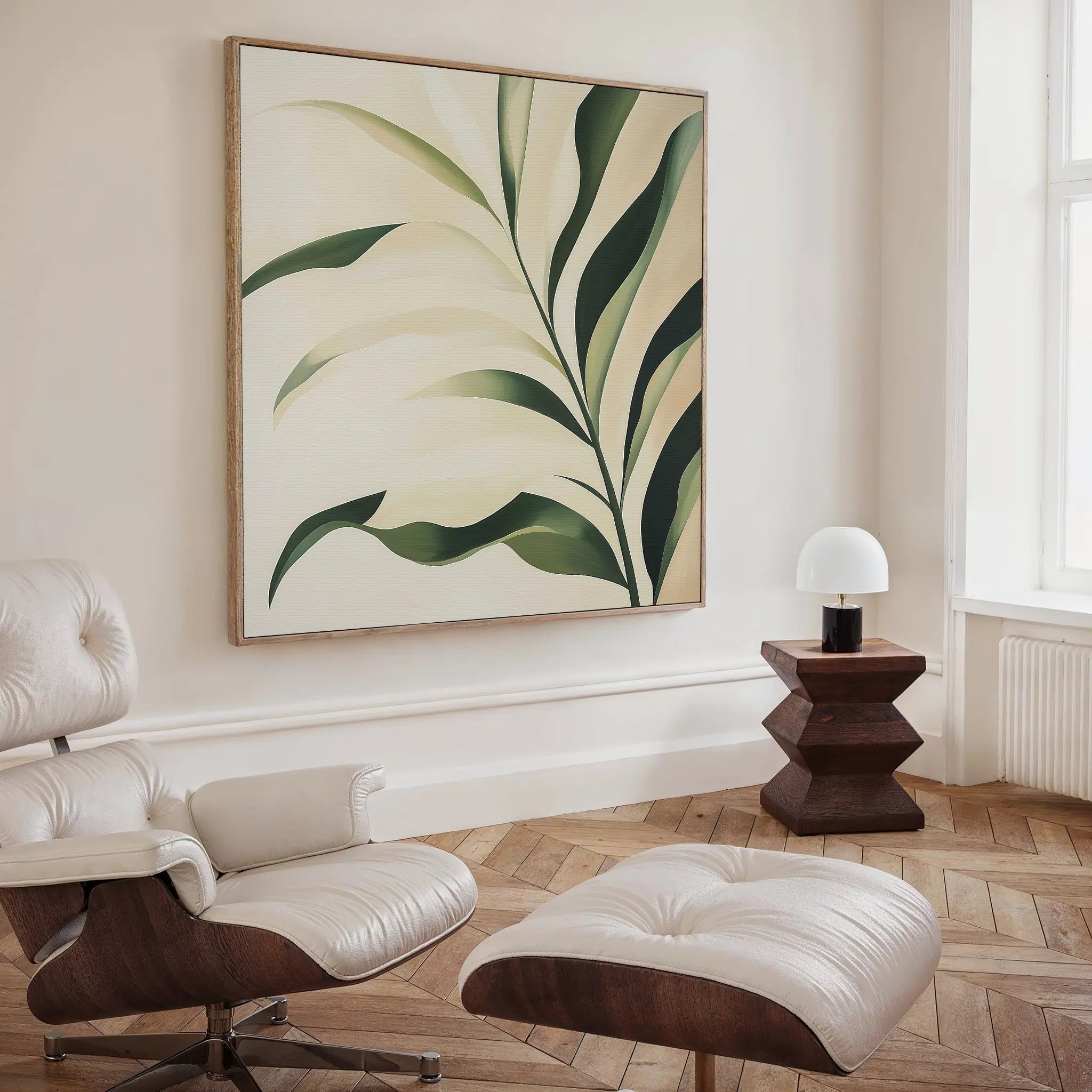 A modern living space with a white leather lounge chair, a geometric wooden side table, and the Spring Foliage Canvas Art—striking botanical wall decor with green leaves on cream that completes any contemporary interior.