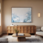 A modern living room with a light wood sideboard with circular patterns, a beige sofa, wooden coffee table, wall sconce, and the Spring Hues Canvas Art – Horizontal in blue and white above—perfect inspiration for stylish decor.