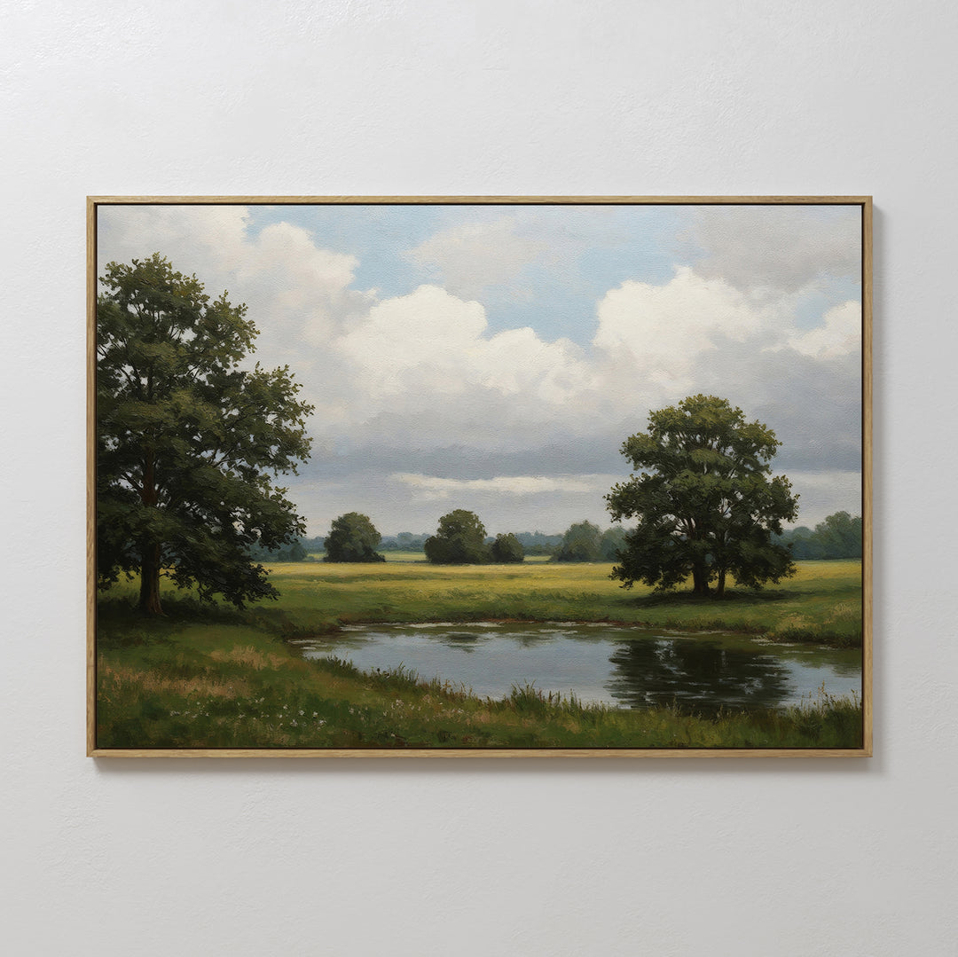 The Still Grove Canvas Art, featuring a serene grassy field, pond, leafy trees, and a cloudy sky, is displayed on a plain white wall.