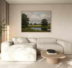 A modern living room with a light beige sectional sofa, wooden coffee table, and the Still Grove Canvas Art—a large landscape painting of trees and a pond—hanging above the sofa. Natural light streams in through curtained windows.