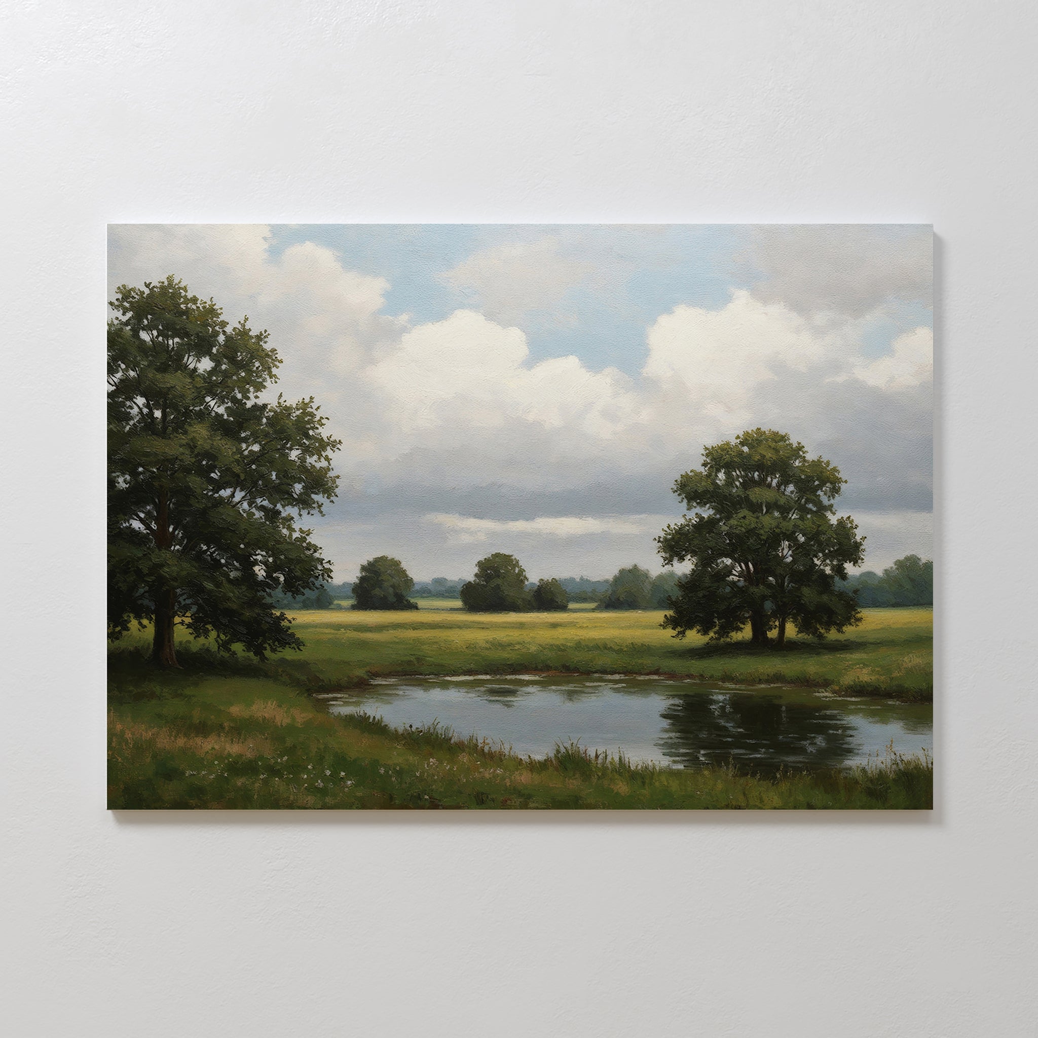 The Still Grove Canvas Art depicts a peaceful pond surrounded by grass and trees beneath a partly cloudy sky, with distant fields in the background, and hangs on a plain light-colored wall.
