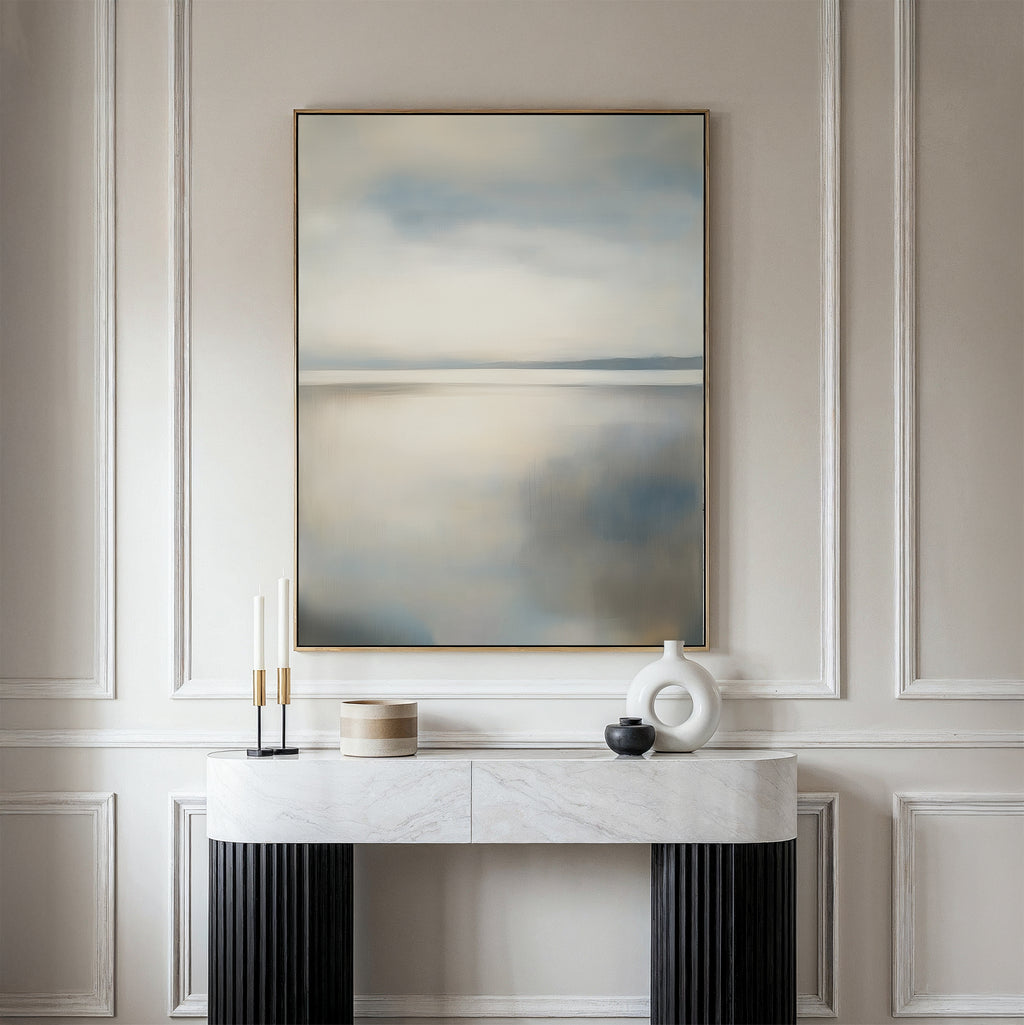 A modern interior features a white console table with minimalist decor against paneled walls. Above, the Still Horizon Canvas Art in soft neutrals adds serene, shoreline-inspired minimalism to the space.