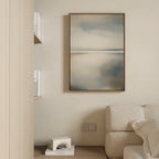 A neutral-toned sofa accents a minimalist living space, complemented by the Still Horizon Canvas Art in soft blue and beige, built-in shelving with books, and a small white decorative object on a wooden surface.