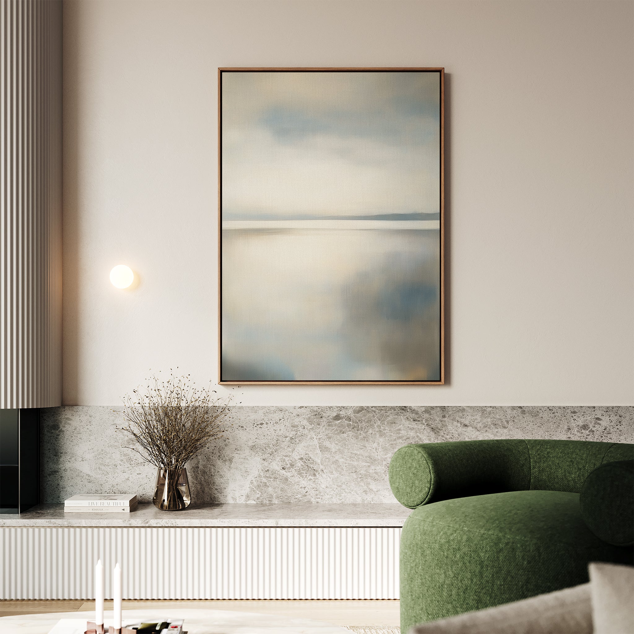 A minimalistic living room featuring the Still Horizon Canvas Art in soft blues and greys, a curved green sofa, built-in shelving with a vase of dried branches, and neutral-toned walls and decor.