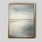Still Horizon Canvas Art: a serene shoreline print with a minimalist landscape in soft blue, gray, and beige hues. Calm water reflects a cloudy sky, all framed in gold with a thin black inner border—perfect minimalist wall art.