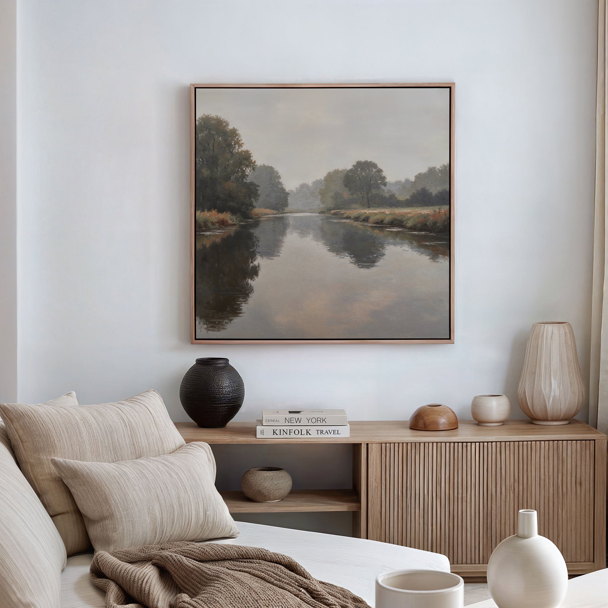 A cozy, neutral-toned living room features a beige sofa, textured cushions, wooden sideboard, decorative vases, and minimalist wall art—a Still Riverbank Canvas Art brings serene elegance to the space.