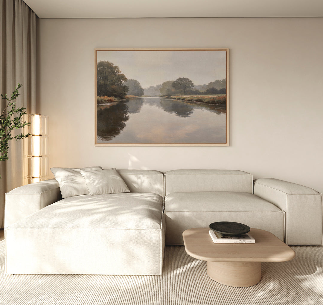A modern living room with a light beige sectional, wooden coffee table with black bowl, and the Still Riverbank Canvas Art – Horizontal on a neutral wall. Natural light brightens the space.