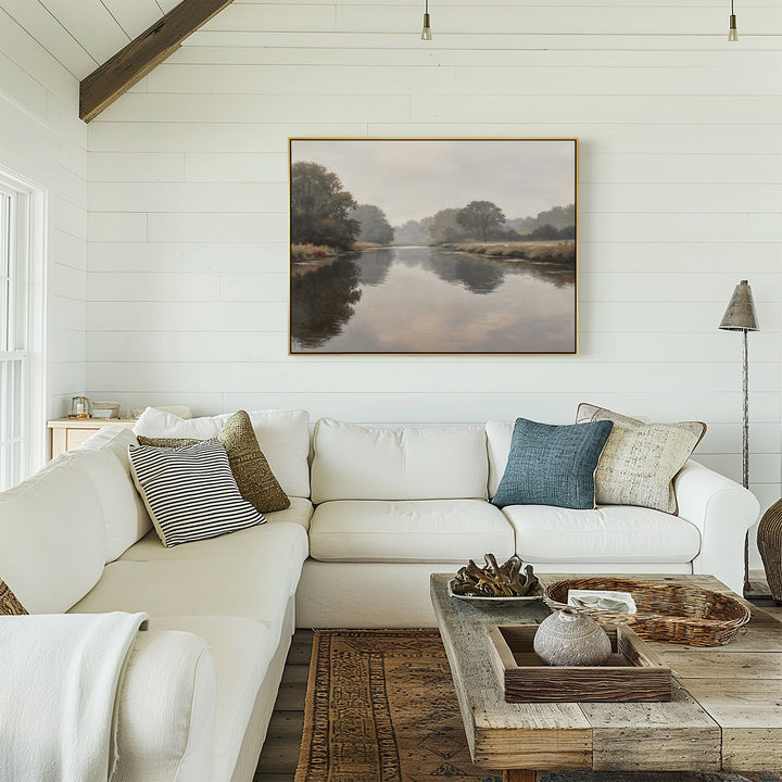 A cozy living room with white shiplap walls, an L-shaped white sofa topped with assorted throw pillows, a rustic wood coffee table, and the Still Riverbank Canvas Art – Horizontal displayed above the sofa.