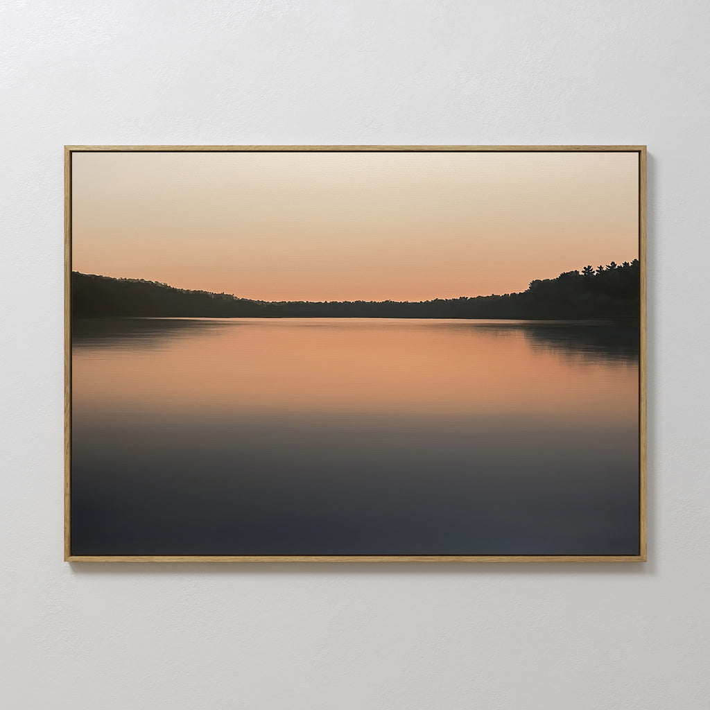 The Still Waters Canvas Art – Horizontal features a tranquil lake at sunset with soft orange and pink hues reflected on the water, dark tree silhouettes lining the horizon—perfect as serene bedroom decor.