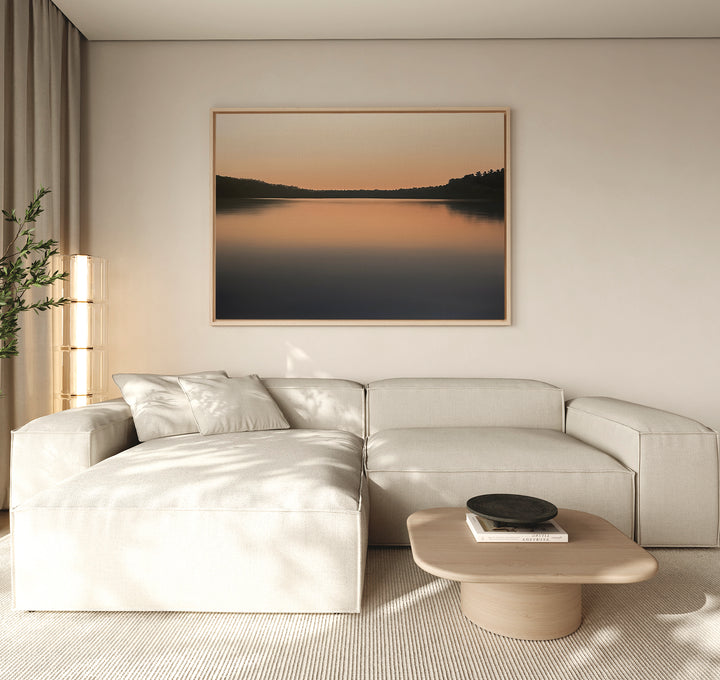 A modern living room with a light beige sectional sofa, low wooden coffee table, and a potted plant. The Still Waters Canvas Art – Horizontal above the sofa and neutral-toned minimal decor create a serene atmosphere.