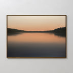 The Still Waters Canvas Art – Horizontal features a tranquil sunset lake scene in soft orange and peach tones with glassy water and silhouetted trees, making it ideal for serene bedroom decor.
