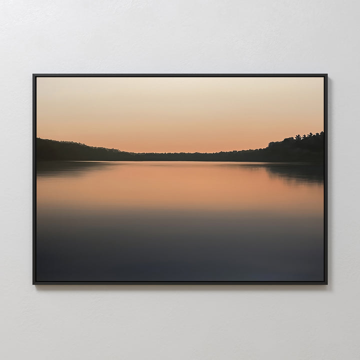 Still Waters Canvas Art – Horizontal: A tranquil canvas print of a calm lake at sunset, with soft orange and peach tones on still waters and dark tree silhouettes—perfect for serene bedroom décor.