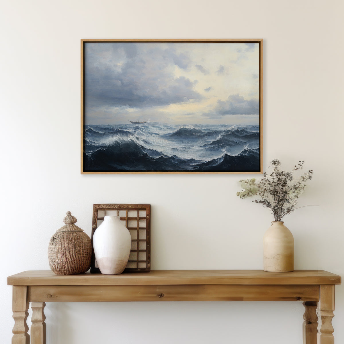 A wooden table with ceramic vases and dried flowers sits beneath the Stormy Seas Canvas Art, which features dramatic waves and a cloudy sky, hanging on a cream-colored wall.