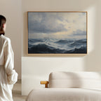 A woman in a white outfit stands in a bright, minimal room, admiring the Stormy Seas Canvas Art featuring ocean waves beneath a cloudy sky, displayed above a beige sofa.