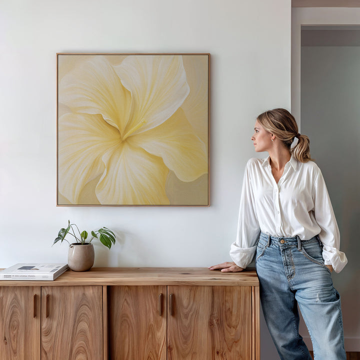 A woman in a white blouse and jeans leans against a wooden cabinet, admiring the Sunlight Curve Canvas Art. A plant and book sit atop the cabinet, enhancing the minimalism of this modern living room decor.