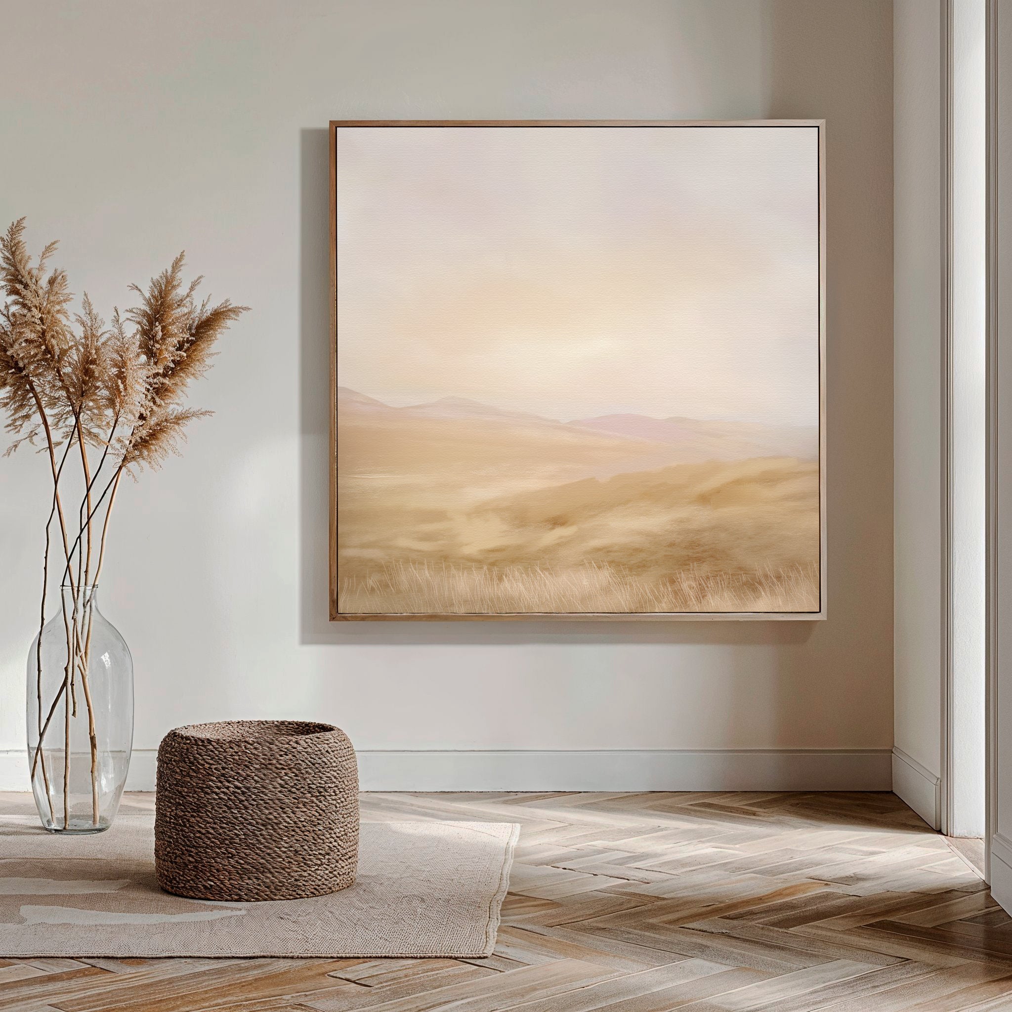 A minimalist room with neutral tones features the Sunlit Meadows Abstract Canvas Art, a clear vase with dried pampas grass, and a woven ottoman on a wooden floor.