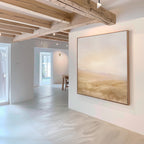 The Sunlit Meadows Abstract Canvas Art hangs on a white wall in a bright, modern room with wooden ceiling beams and natural light. Minimalist decor and wood accents complement the soft tones of this airy landscape artwork.