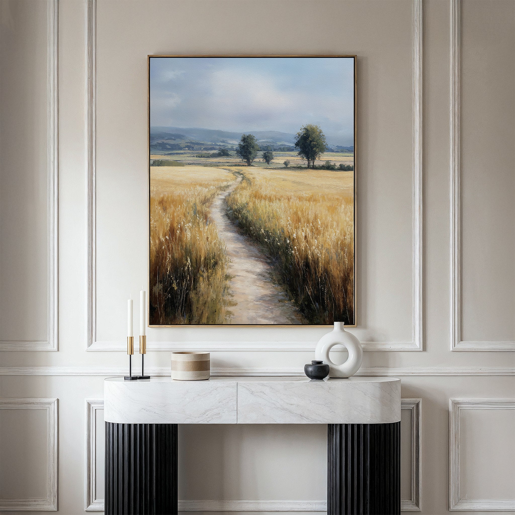 A marble console table with modern decor sits against a white paneled wall. Above it hangs the Sunlit Passage Canvas Art, depicting a country path winding through golden fields toward distant trees and hills under a blue sky.