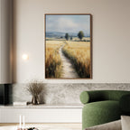 A living room with a green sofa and large wall art—the Sunlit Passage Canvas Art, featuring a rural landscape of golden fields, a winding path, distant trees, and soft hills beneath a cloudy sky.