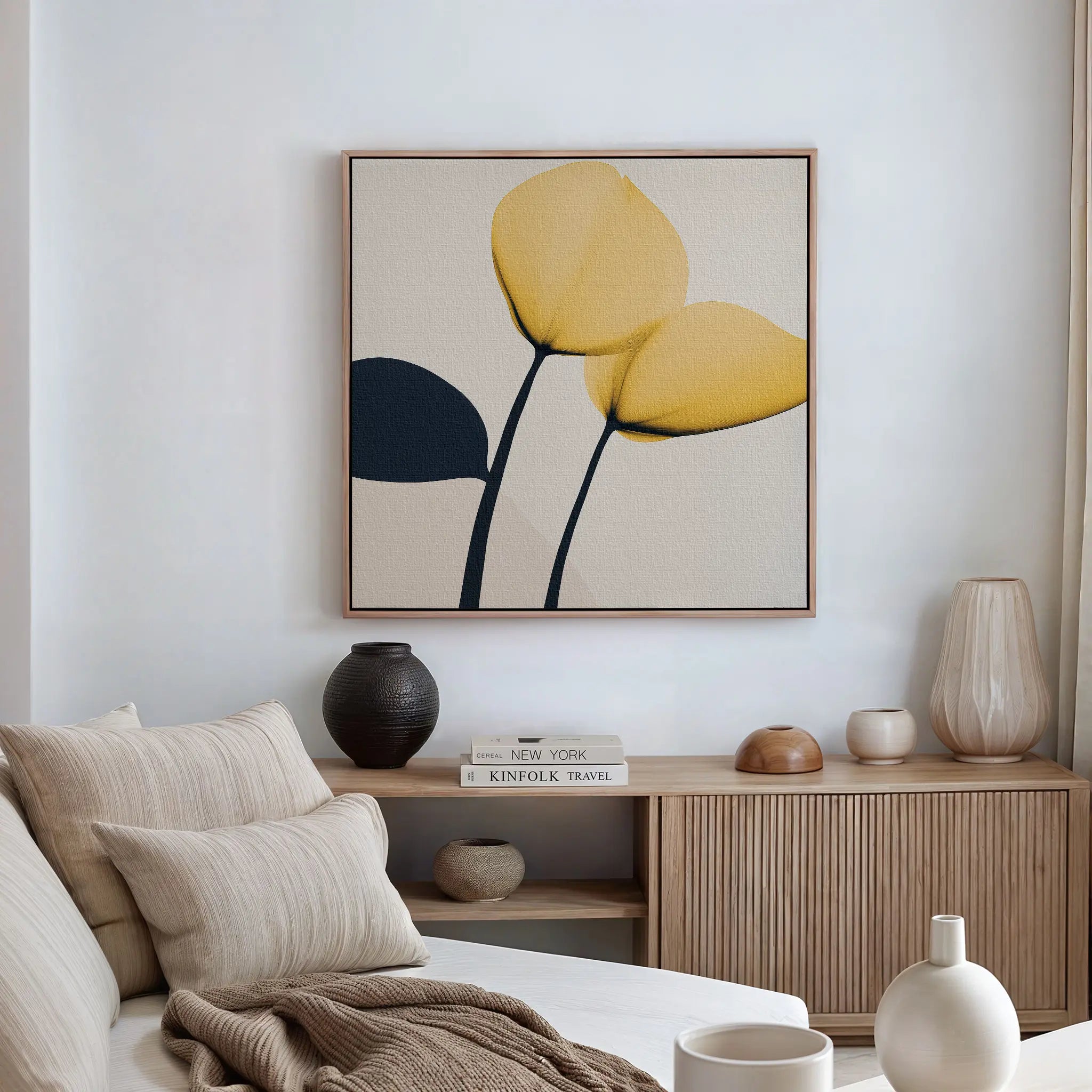 A modern living room with a beige sofa, neutral cushions, wooden sideboard, decorative vases, stacked books, and the Sunny Flora Canvas Art—striking floral wall art featuring three yellow blooms—framed on the wall.