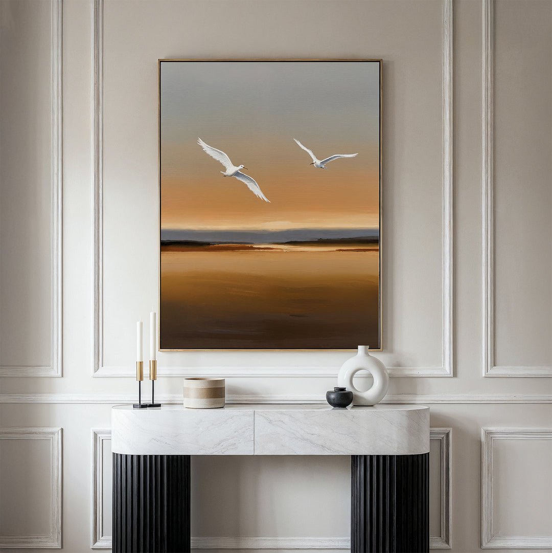 A minimalist room features a marble console table, modern decor, and the Sunset Flight Canvas Art—a large minimalist wall piece with two white birds soaring over a brown and orange landscape, ideal for contemporary bedroom decor.