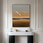 A minimalist room features a marble console table, modern decor, and the Sunset Flight Canvas Art—a large minimalist wall piece with two white birds soaring over a brown and orange landscape, ideal for contemporary bedroom decor.