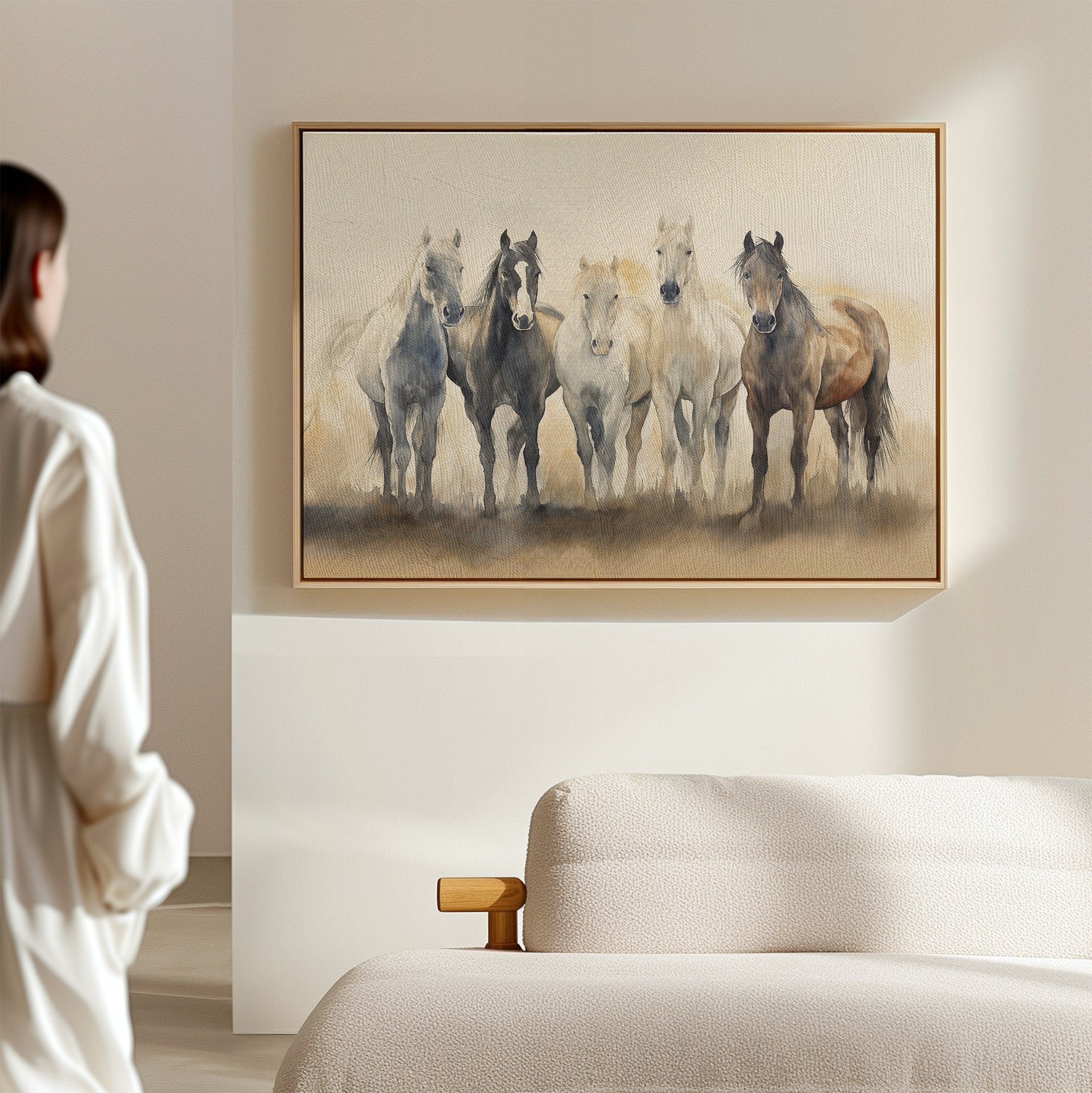 A person in a white robe stands in a softly lit, minimal room, admiring the Sunset Ride Canvas Art above a light-colored sofa—a perfect addition to nature-inspired living room decor.