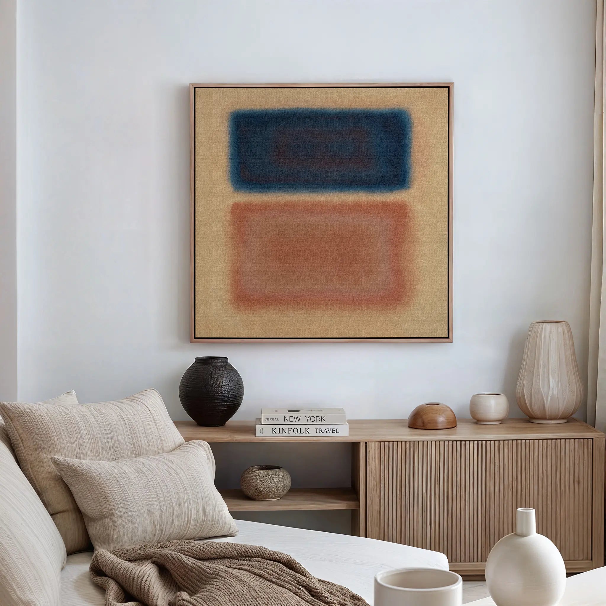 A minimalist beige living room featuring a sofa with striped cushions, a wooden sideboard with ceramic vases and books, and modern interiors highlighted by the Sunset Vapor Canvas Art of blue and reddish-brown rectangles on the wall.