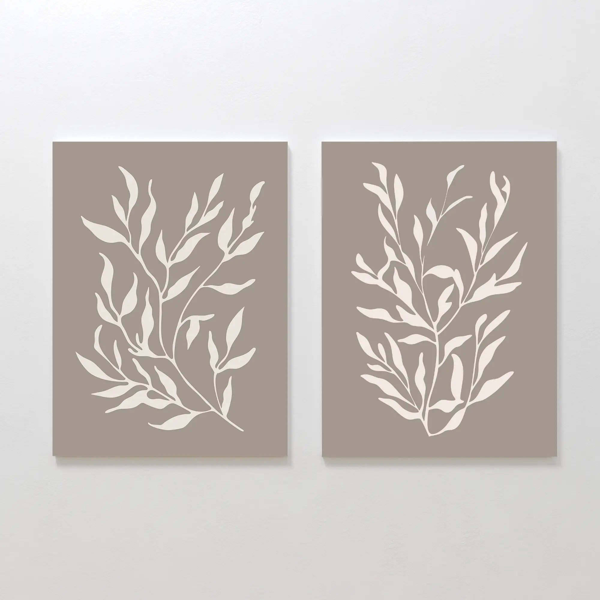 The Taupe Botanical Set of 2 features taupe canvas prints with minimalist white leaf designs, perfect for hanging side by side on a white wall. Their modern style enhances contemporary interiors with elegant symmetry.