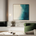 A modern living room featuring Teal Tide Canvas Art, a round green armchair, a low marble shelf, a vase with dried branches, and stacked books with candles on a white coffee table.