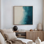 A modern living room with a beige sofa, neutral pillows, a wooden sideboard topped with decor, and the Teal Tide Canvas Art featuring blue and cream tones displayed on the wall.