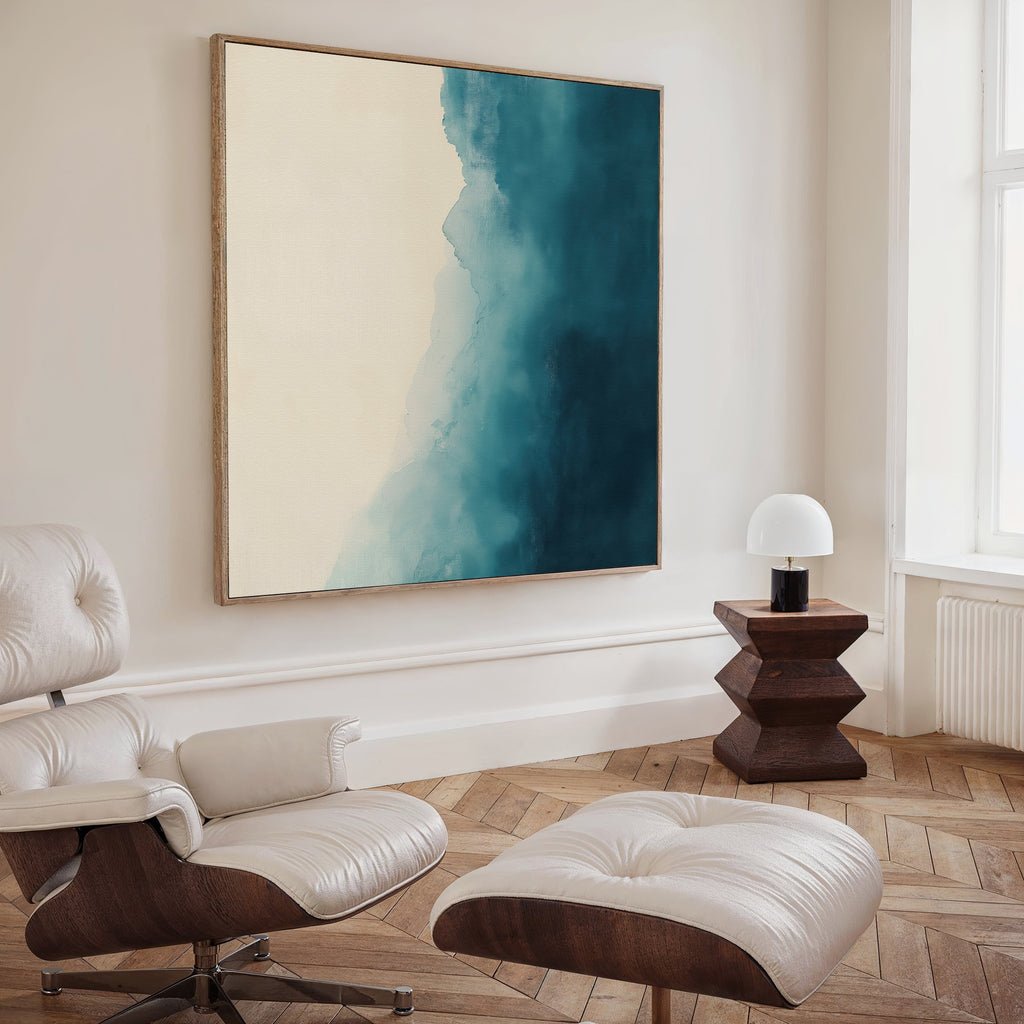 A modern living room with a white leather lounge chair and ottoman, wooden side table with a white lamp, Teal Tide Canvas Art in blue and cream tones on the wall, light wood herringbone floor, and a large window.
