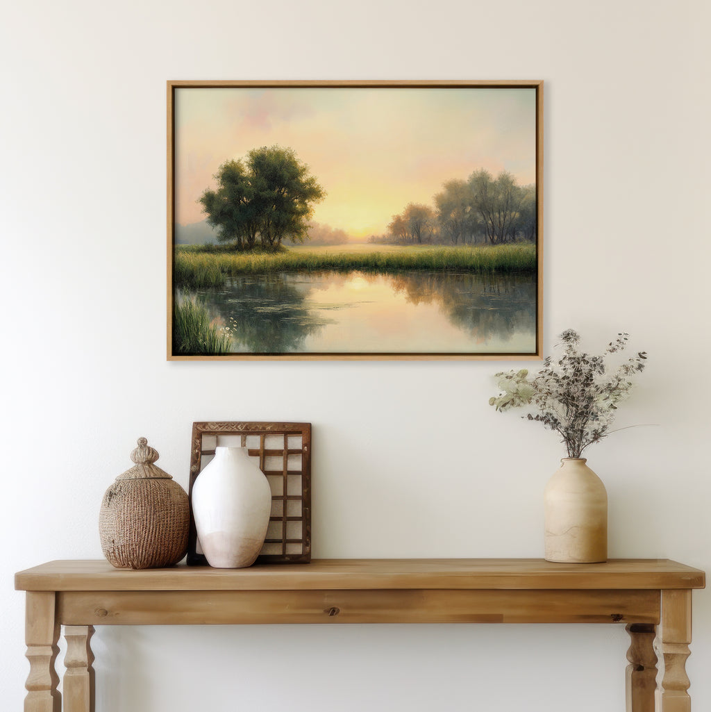A wooden table with vases and dried flowers sits beneath The Journey Canvas Art—a landscape of trees and a calm lake at sunset—bringing countryside charm to the white wall.