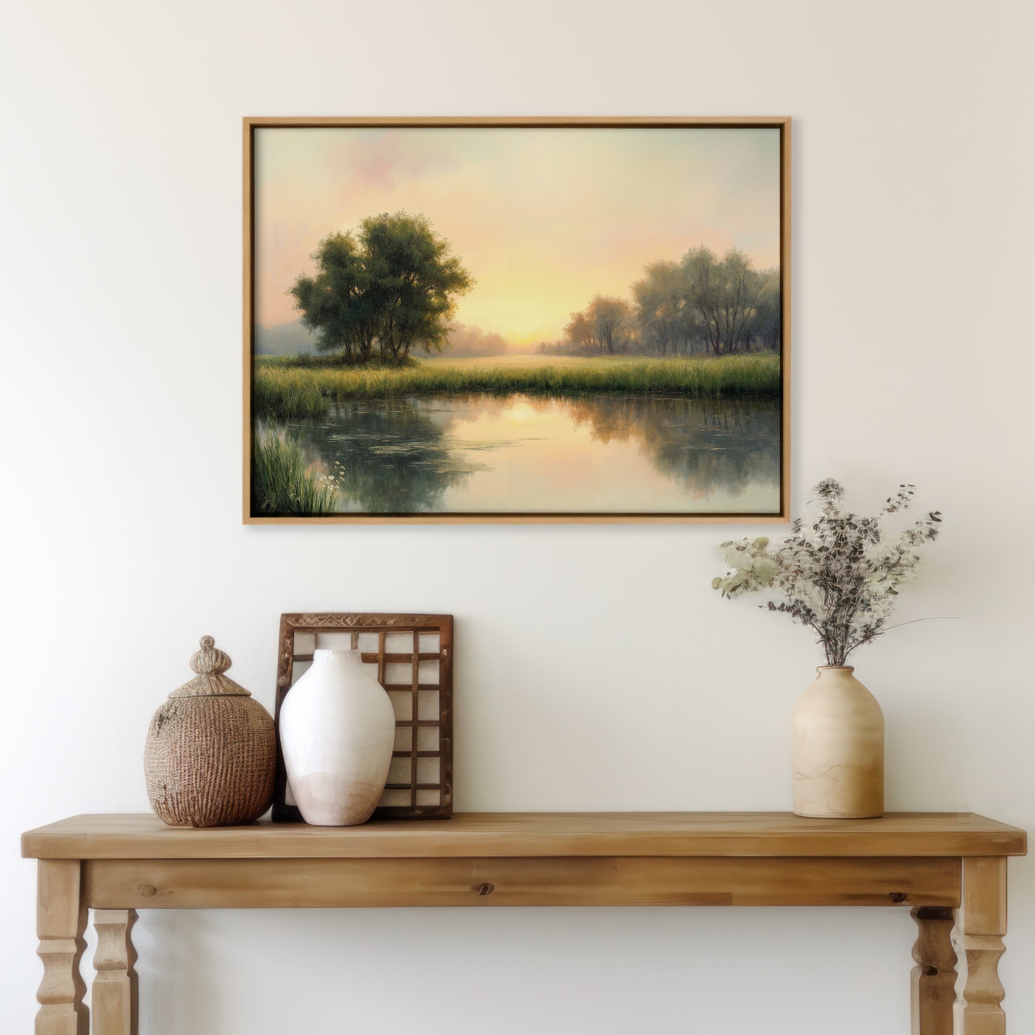 A wooden table with vases and dried flowers sits beneath The Journey Canvas Art—a landscape of trees and a calm lake at sunset—bringing countryside charm to the white wall.