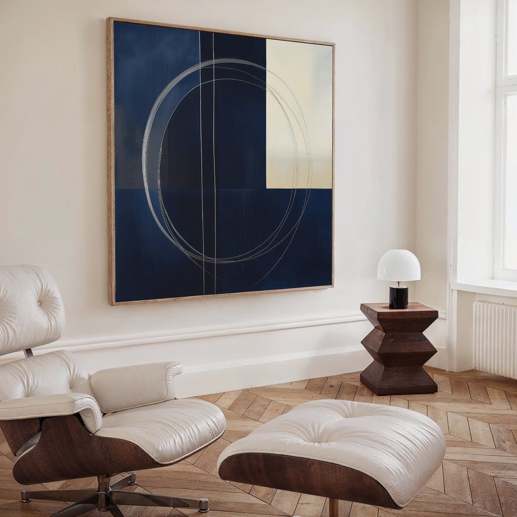 A modern living room features a white leather lounge chair and ottoman, a wooden side table with dome lamp, herringbone wood floors, and The Orbit Canvas Art in blue and cream tones—perfect for fans of modern home decor.
