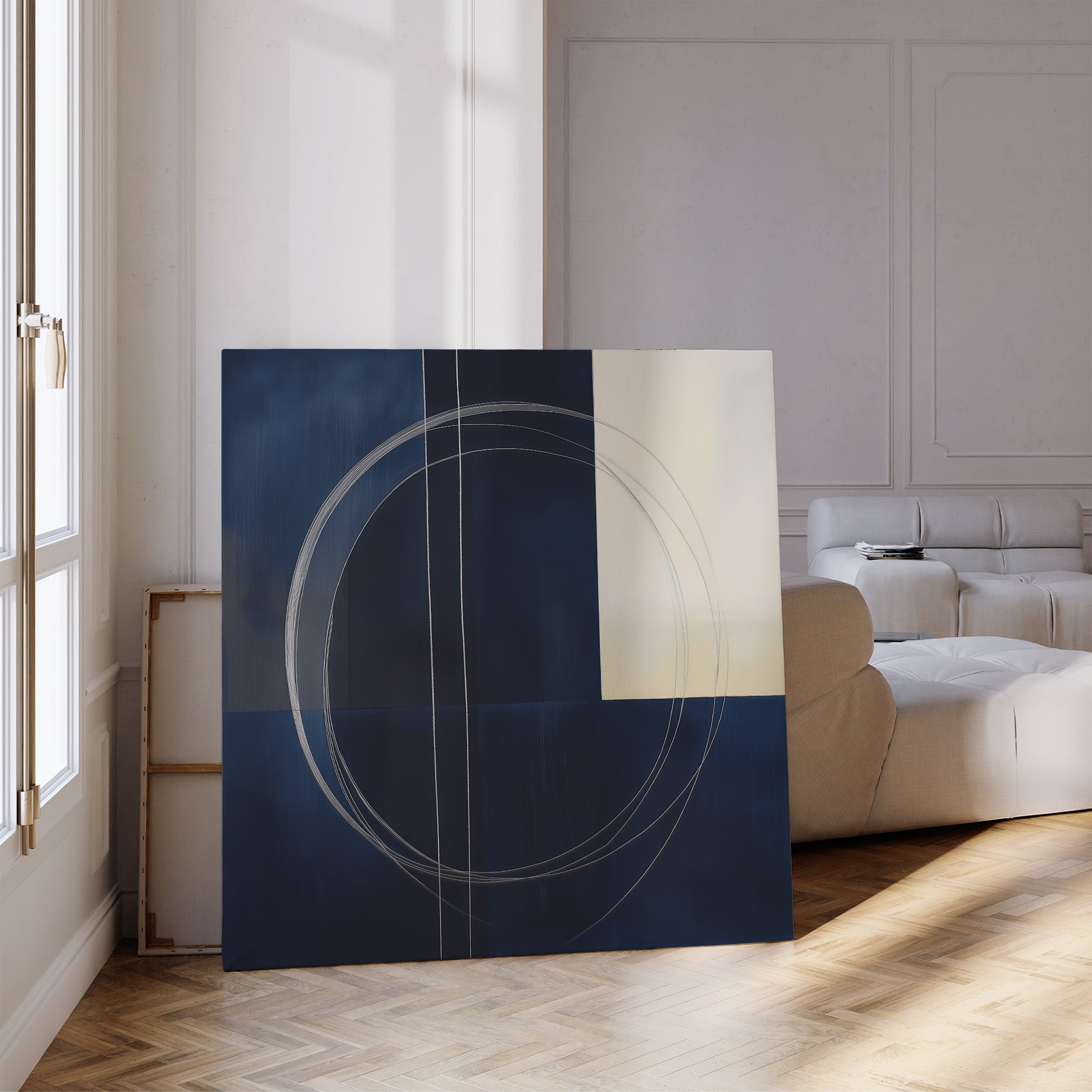 A modern living room with light walls showcases The Orbit Canvas Art, featuring navy, cream, and geometric shapes with intersecting circular lines. Sunlight streams through tall windows, highlighting the contemporary decor.