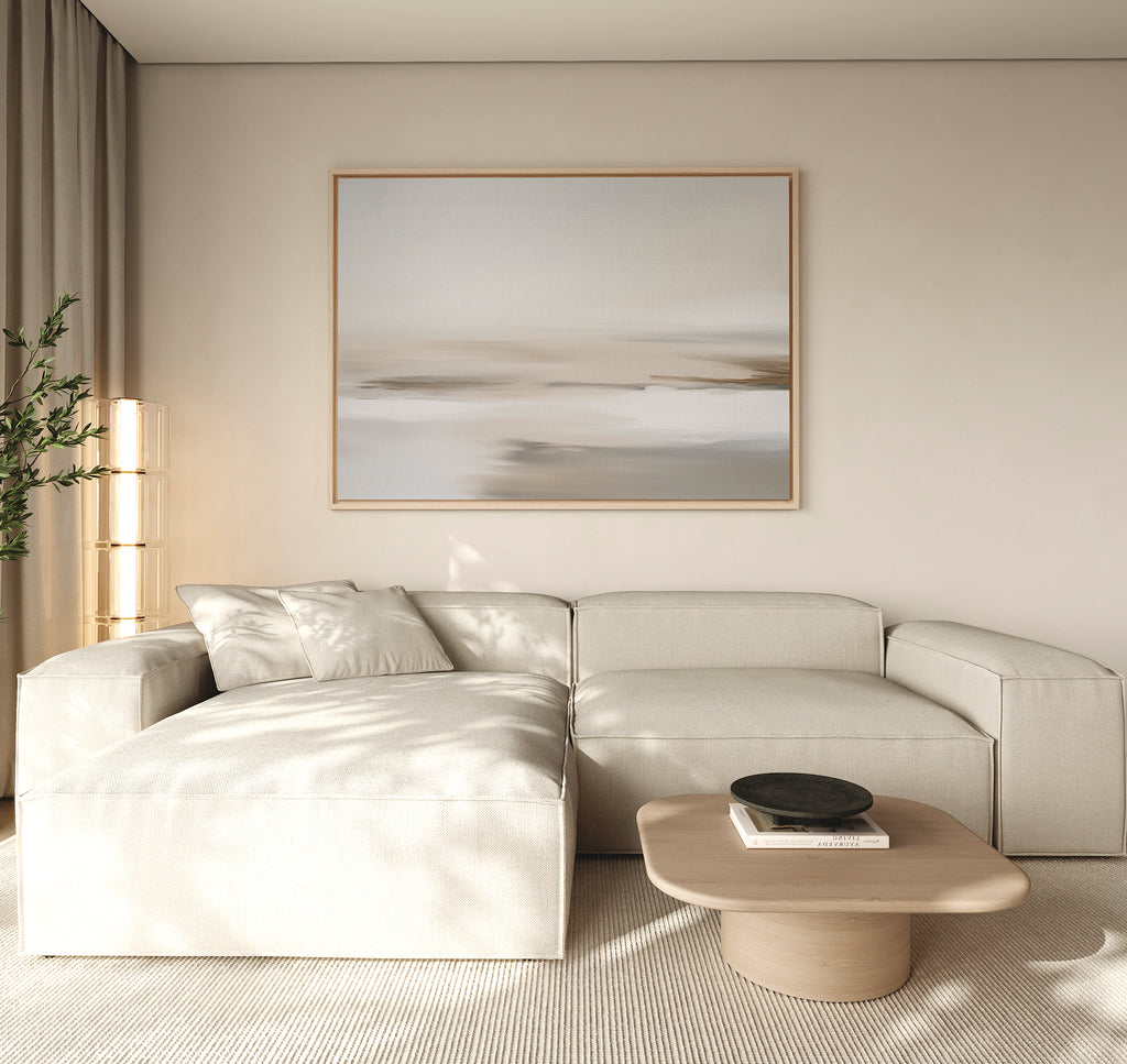 A minimalist living room features a light beige sectional sofa, a low wooden coffee table with a black bowl, tall curtains, soft natural light, and the Tranquil Shifts Canvas Art – Horizontal as modern wall art.