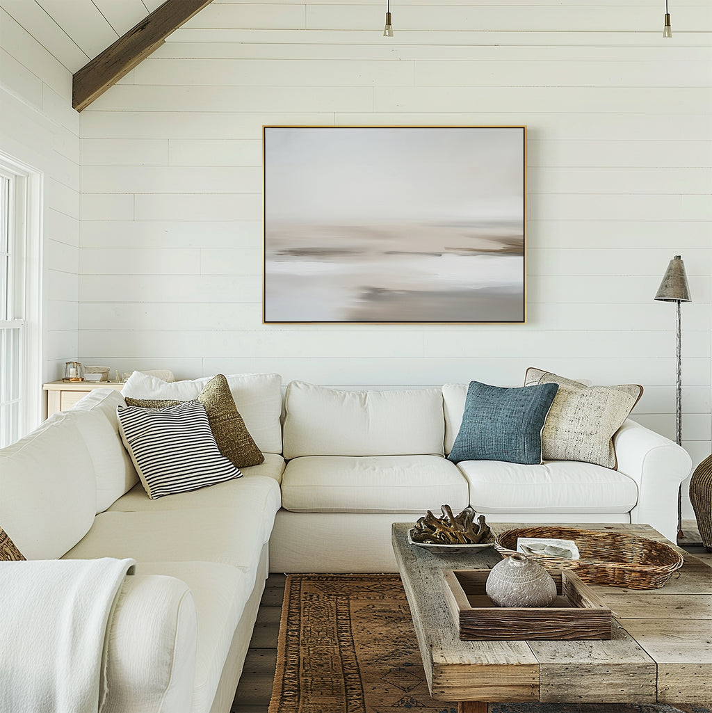 A cozy living room with white shiplap walls, a white sectional sofa with assorted pillows, a rustic wooden coffee table, decorative trays and vases, and the Tranquil Shifts Canvas Art – Horizontal framed above the couch enhances the inviting decor.