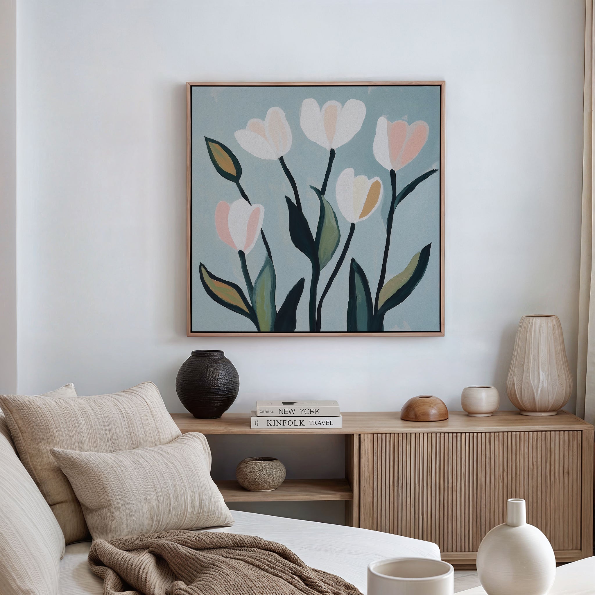 A cozy, minimal living room with a light wood sideboard, neutral decor, books, and minimalist wall art—Tulip Harmony Canvas Art—above a beige sofa with striped pillows, perfect for elegant living room decor.
