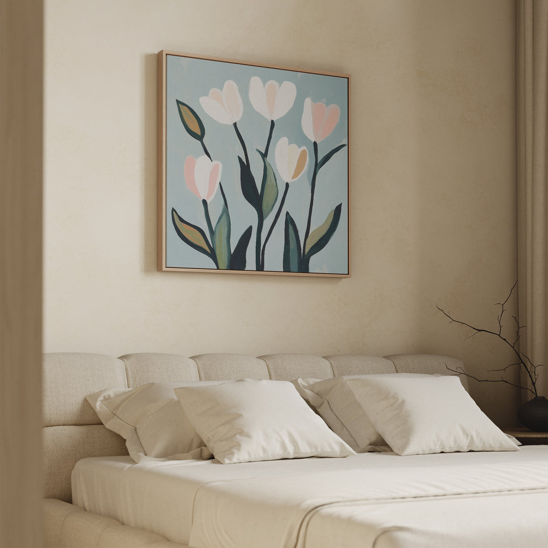A beige bed with white pillows and bedding sits against a light wall. Above the bed hangs Tulip Harmony Canvas Art—minimalist wall decor featuring abstract tulips with light pink petals and green leaves on a blue background.