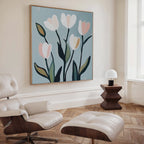 A modern living room showcases a white leather lounge chair and ottoman, wooden side table with a small white lamp, and Tulip Harmony Canvas Art—a floral painting with abstract tulips on blue—perfect for stylish living room decor.