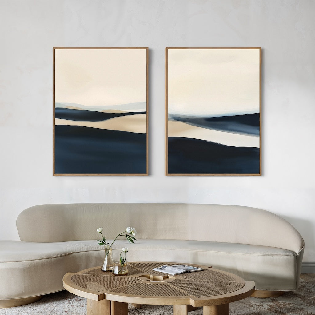 A modern living room features a curved beige sofa, a round wooden coffee table with vases and books, and the Twilight Horizons Set of 2 abstract landscape paintings in neutral tones above the sofa—creating an elegant, inviting space.