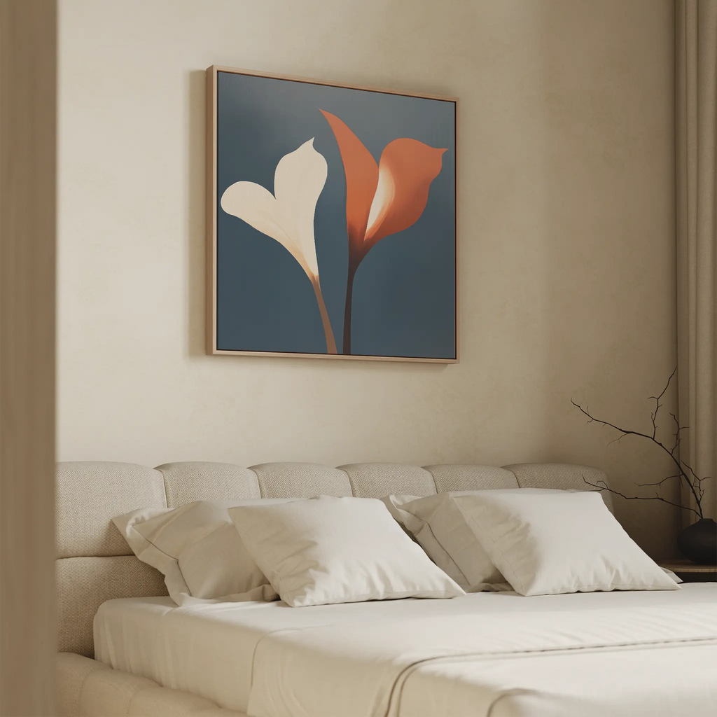 A minimalistic bedroom features a beige bed with four white pillows. Above, the Twin Blooms Canvas Art from Nordic Park displays two calla lilies—one white, one red—set against a dark blue background for striking wall decor.
