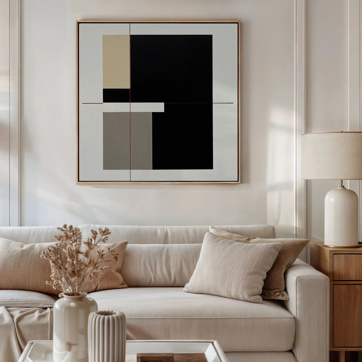 A modern living room with a beige sofa, neutral-toned cushions, a side table with a ceramic lamp, dried flowers in a vase, and striking Urban Balance Canvas Art featuring black-and-white geometric designs.